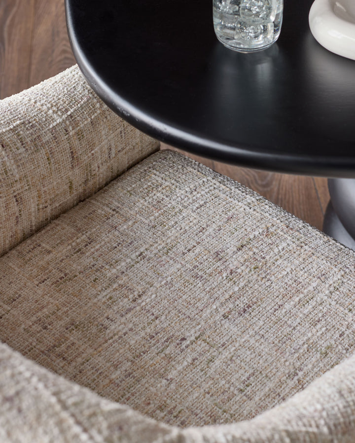 Freya dining chair in natural fabric, showing close-up of woven upholstery texture with black round table and glass of water nearby.