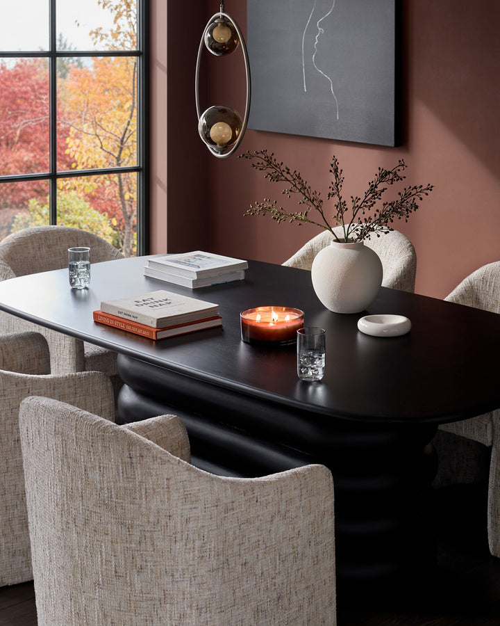 Freya dining chair in natural fabric, shown at black dining table in warm interior setting with autumn views.