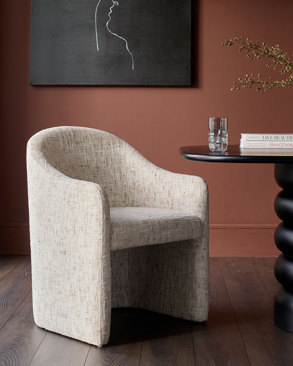 Freya dining chair in natural fabric, barrel-shaped design with curved arms and back, displayed in terracotta room setting.