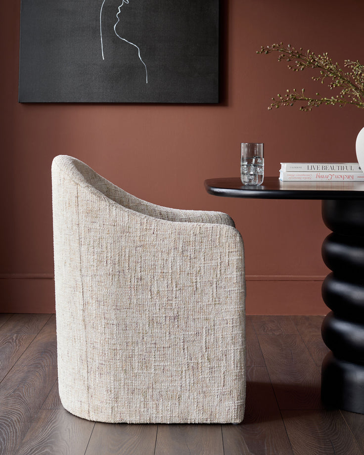 Freya dining chair in natural fabric, curved backrest, side view in terracotta room setting.