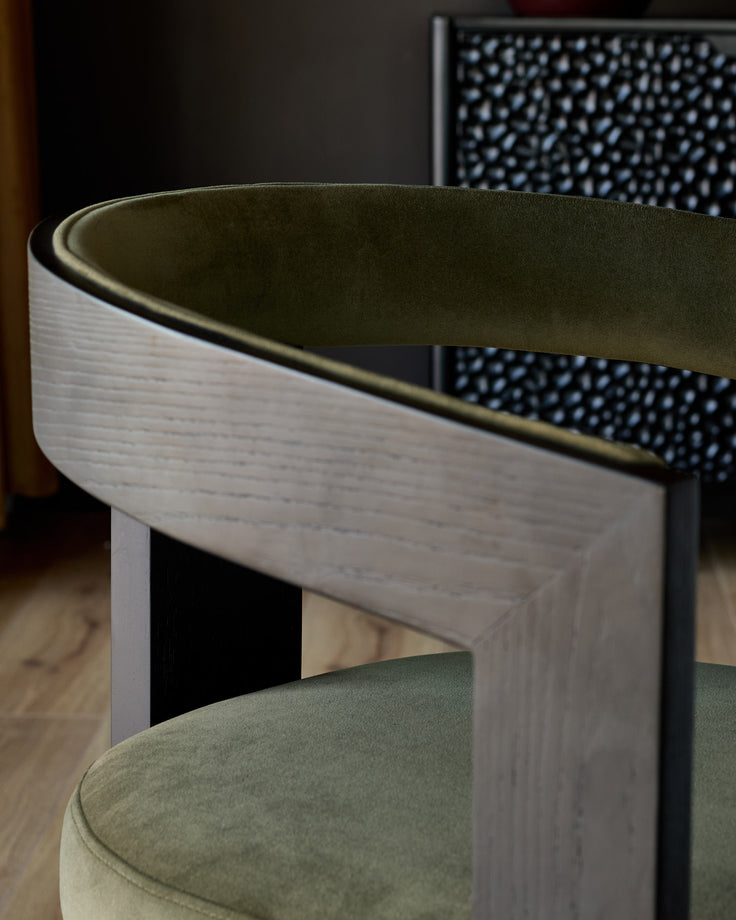 Garcia dining chair in olive green velvet, side view showing curved backrest and light wood frame detail.