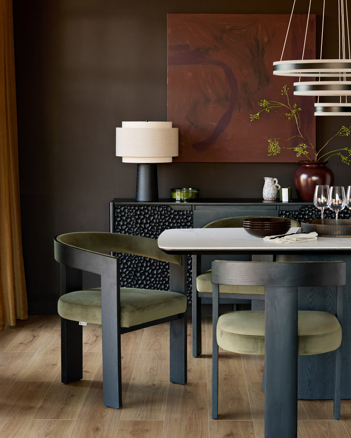 Garcia dining chair in olive green velvet with curved wooden backrest, shown at dining table.