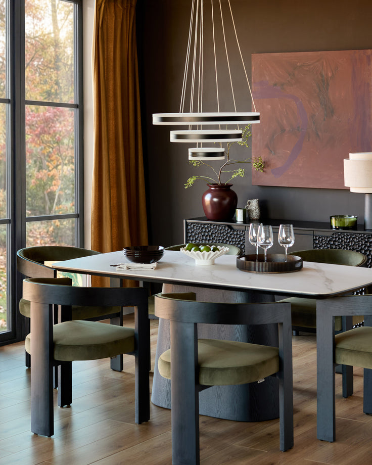 Garcia dining chair in olive green velvet, shown tucked under a marble-top table in a modern dining room setting.