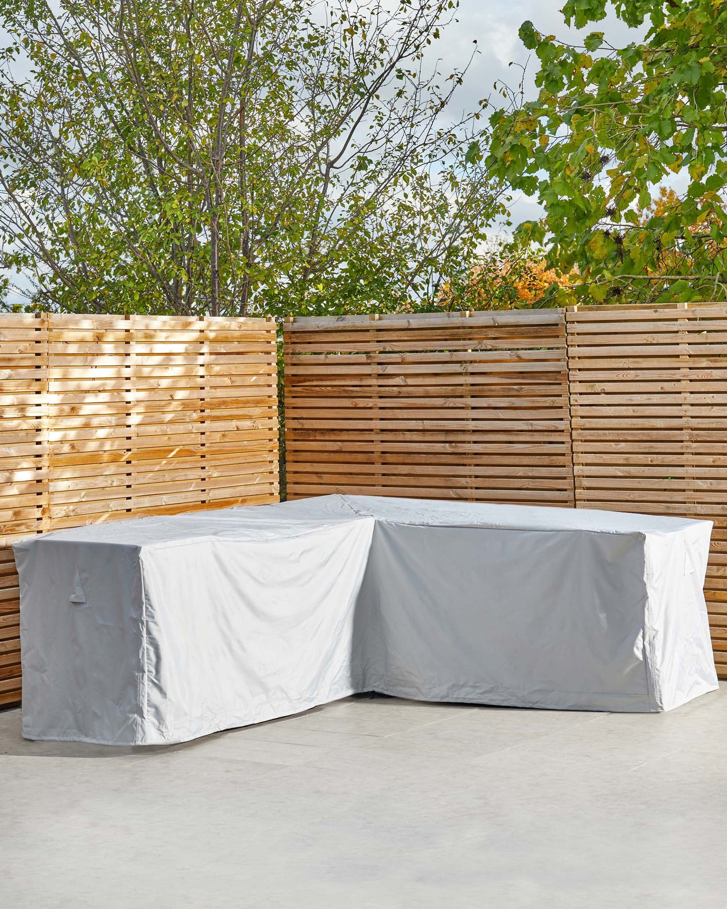 Large L-shaped outdoor dining set cover in Grey and white, displayed on patio with wooden fence and trees.