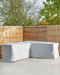 A covered outdoor sectional sofa in a minimalist setting, surrounded by wooden slat fencing and greenery.