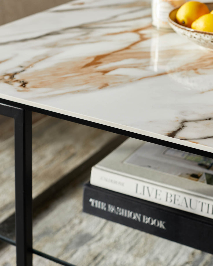 Marble-effect table with black frame and shelf holding coffee table books and a bowl of lemons.