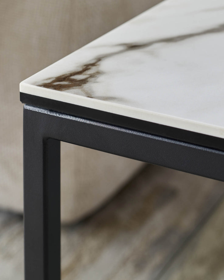 Close-up of a stylish side table. Features a faux marble top, black trim, and sleek metal legs. Modern design.