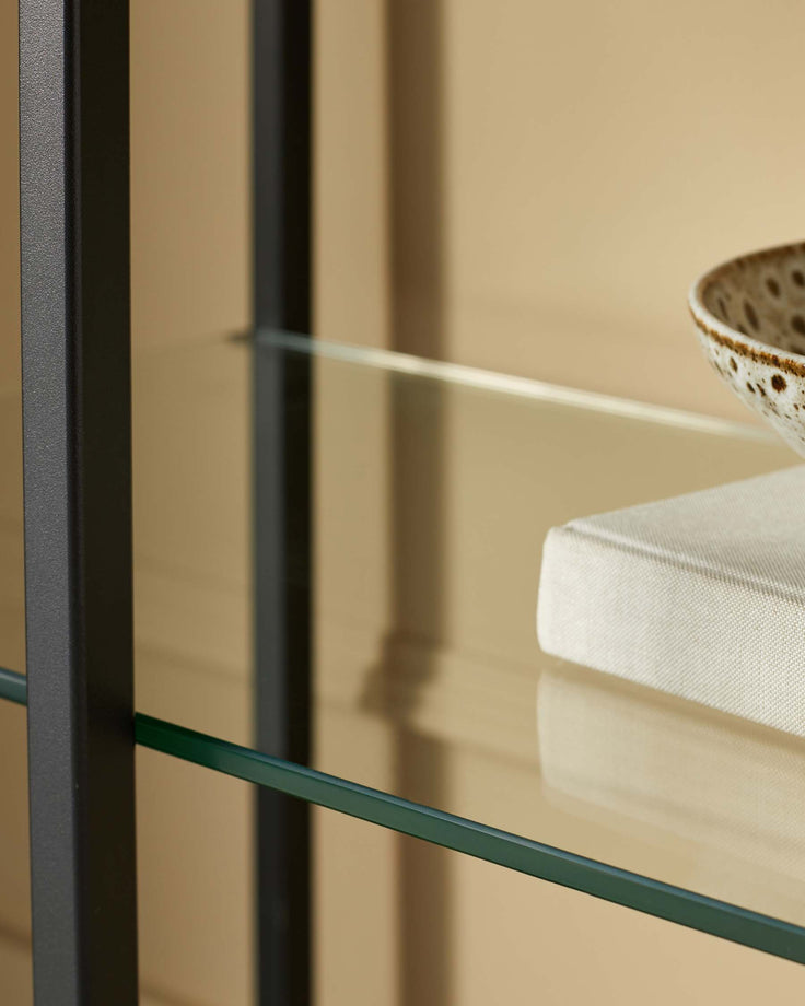 Close-up of a sleek, dark-framed shelving unit with glass shelves, displaying neutral-toned decor.