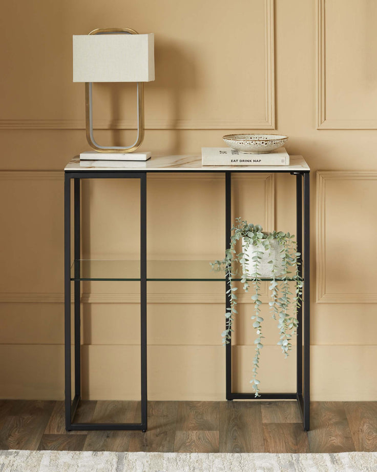 Console table with black frame, glass shelf, marble top, lamp, plant and books. Elegant storage for any hallway or living space.