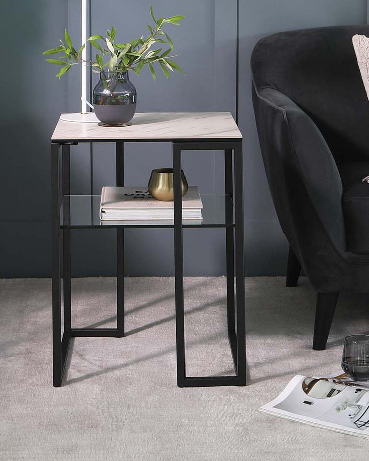 Modern side table with a marble top, black metal frame, lower glass shelf, and decorative accents like a vase and candle.