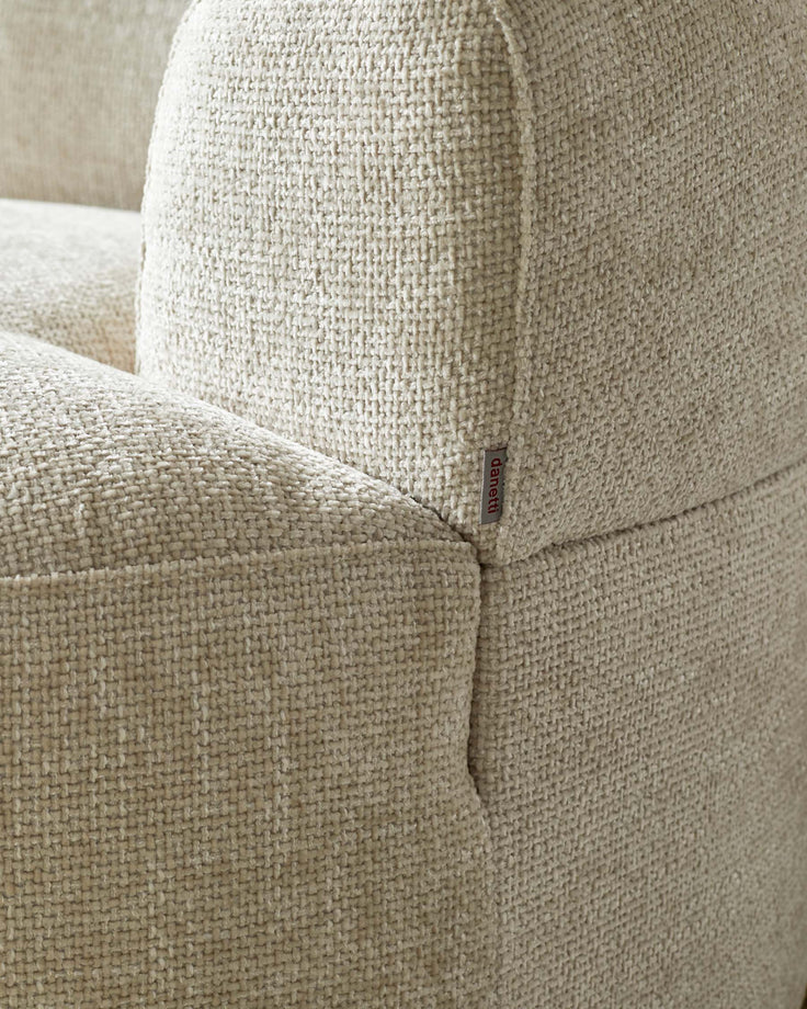 Cream textured upholstery of a contemporary sofa, featuring rounded edges and a subtle brand tag.