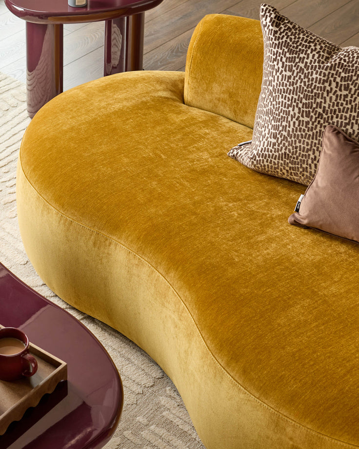 Ochre Gianna 2-seater sofa with curved design, upholstered in textured fabric, styled with patterned and tan pillows.