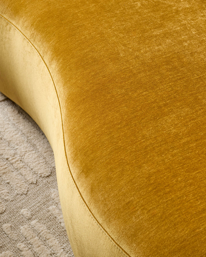 Gianna 2-seater sofa in ochre fabric, close-up detail showing curved armrest and textured weave against neutral carpet.