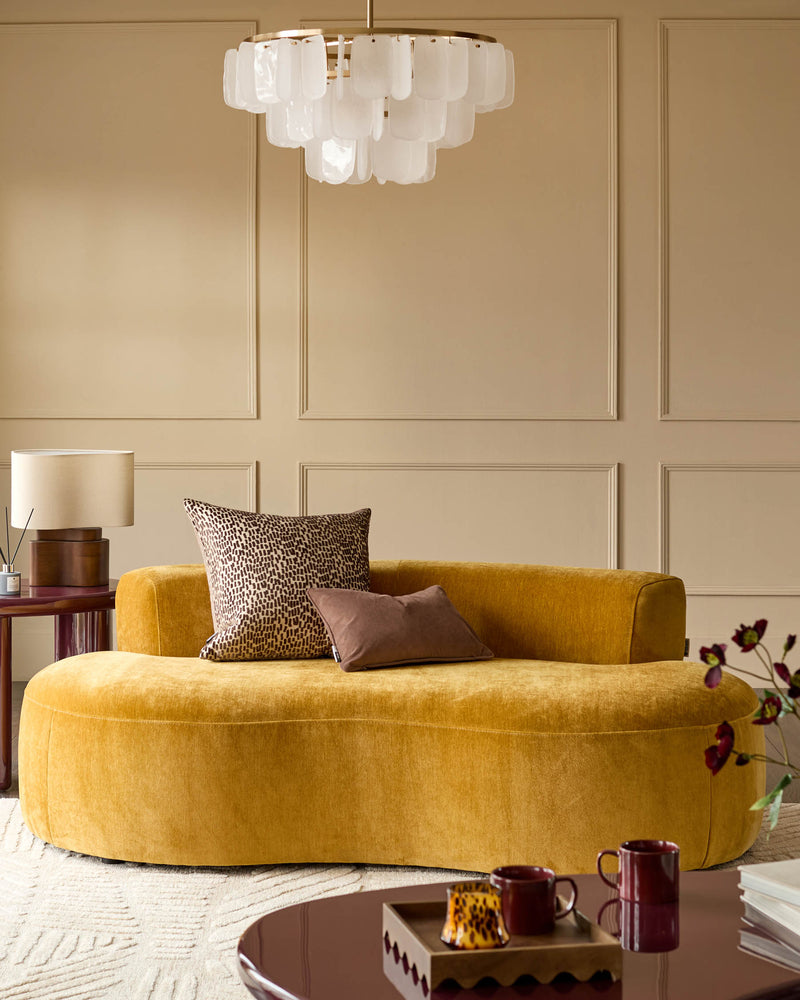 Gianna 2-seater sofa in ochre fabric with curved design, styled in a neutral beige room with decorative pillows.