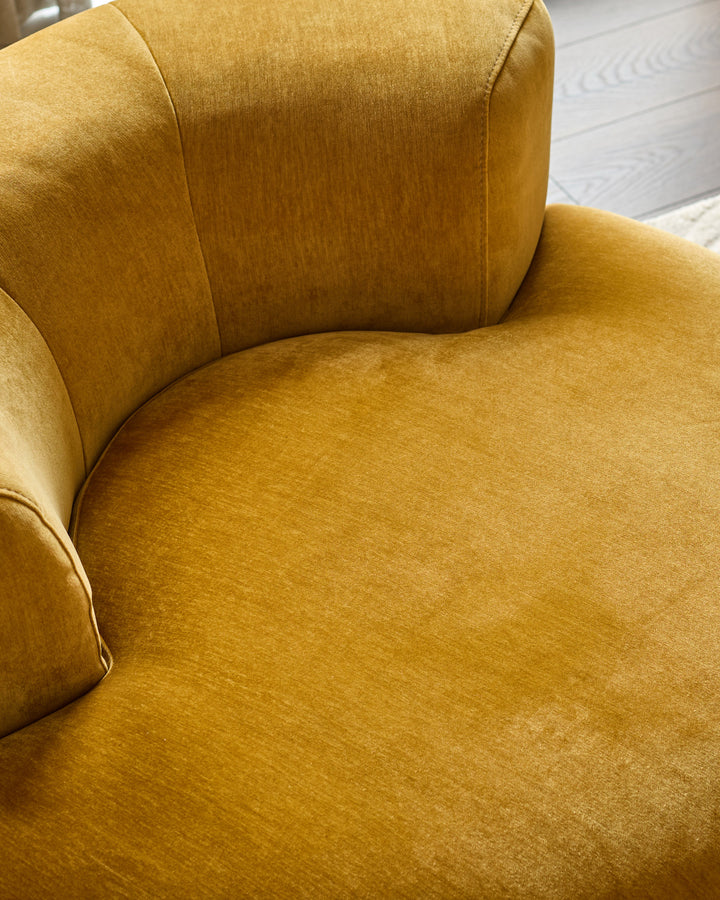Gianna armchair in ochre fabric, showing curved backrest and seat cushion from above, displayed on light wood flooring.