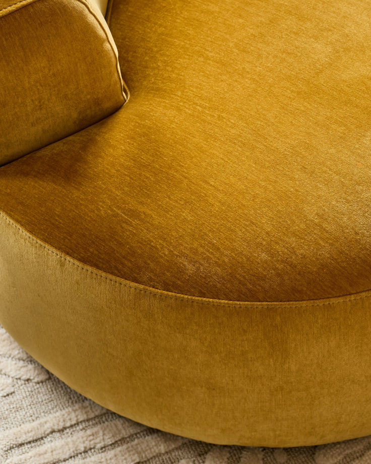 Ochre fabric armchair with curved rounded back and seat, shown from above on a neutral striped rug.
