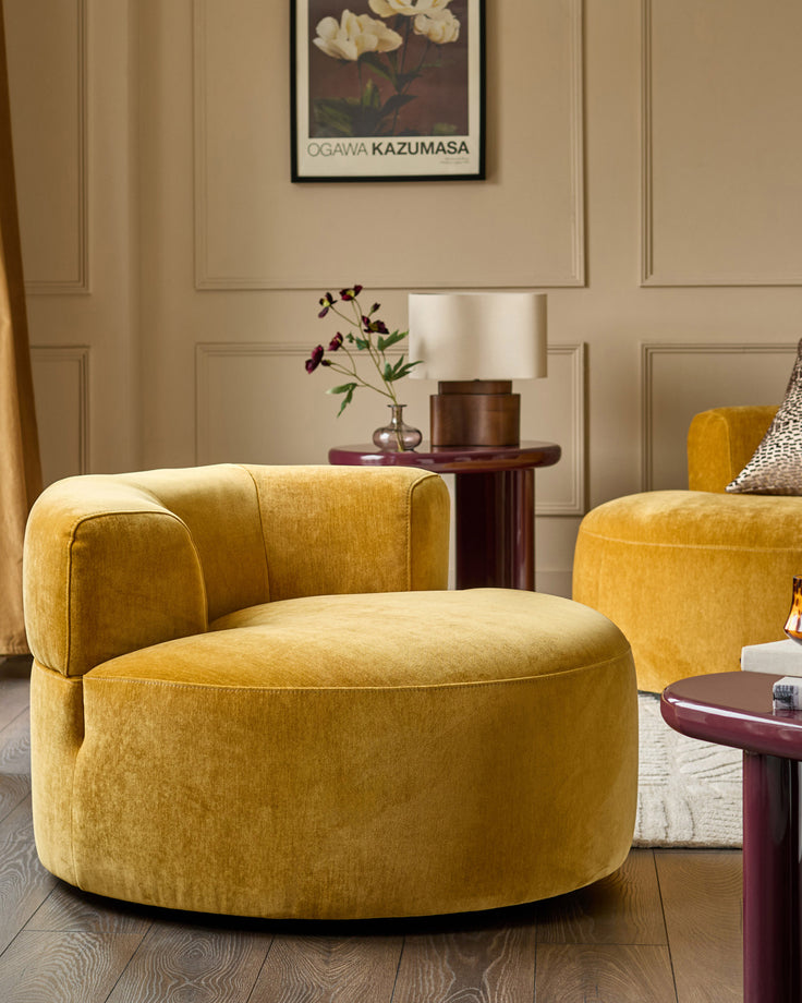 Gianna armchair in ochre fabric with curved barrel shape, rounded back, and black base in a styled living room setting.