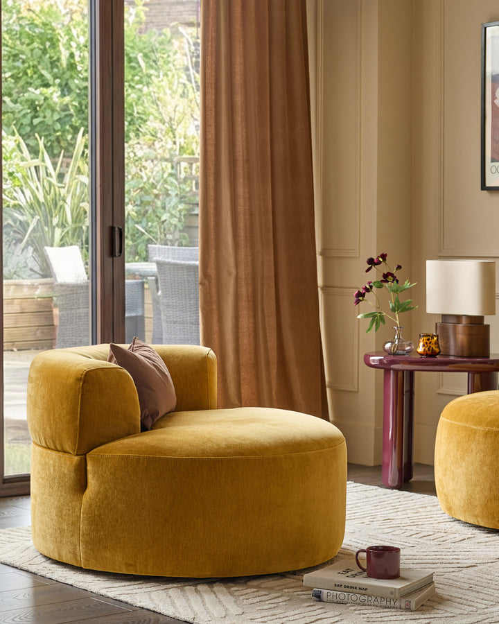 Gianna armchair in ochre fabric, showcased in a styled living room with matching ottoman and wooden side table.