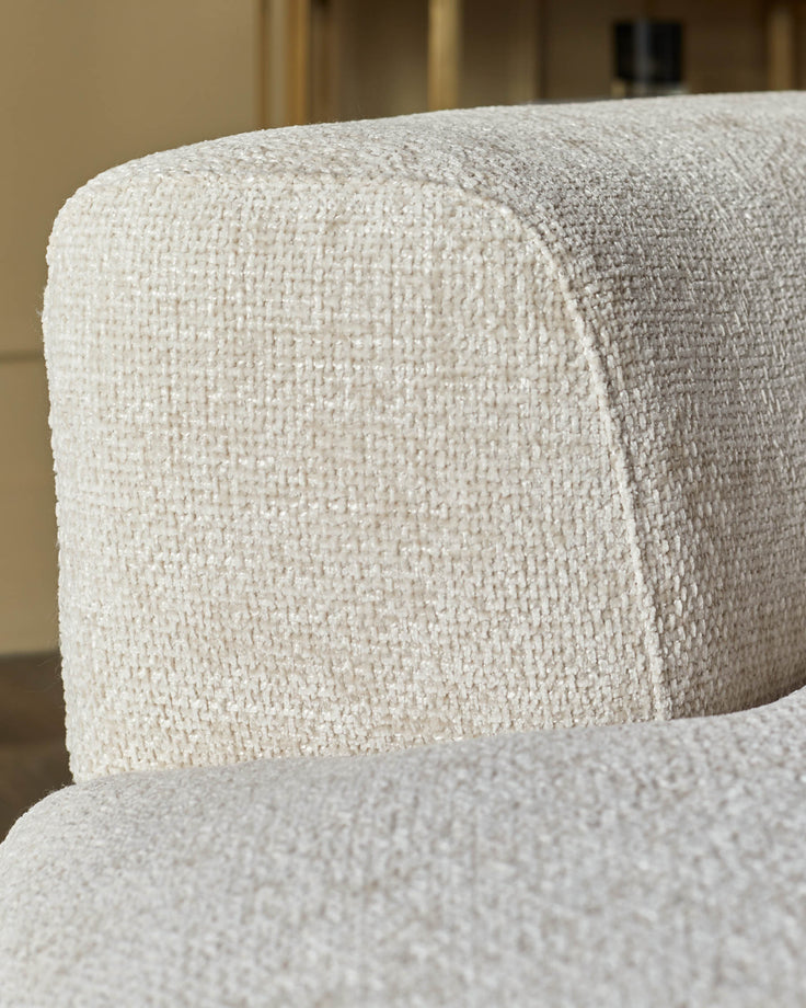 Close-up of an armchair showing its textured, cream fabric and curved design, lending a luxurious feel.