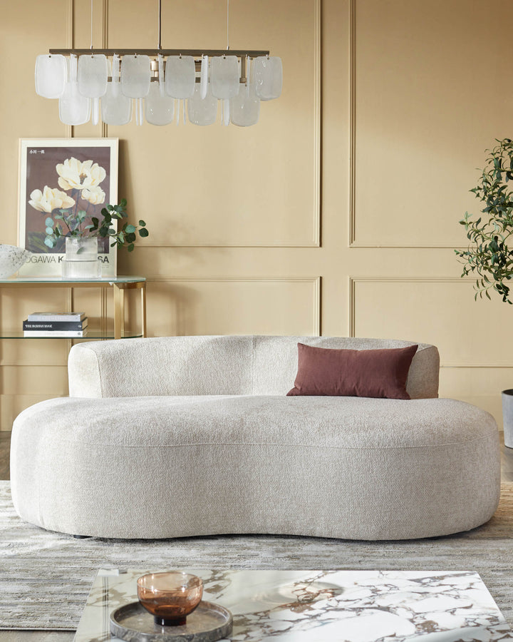 A curvy, neutral-toned sofa with a brown cushion. Glass-topped tables and a modern chandelier complete the living room scene.