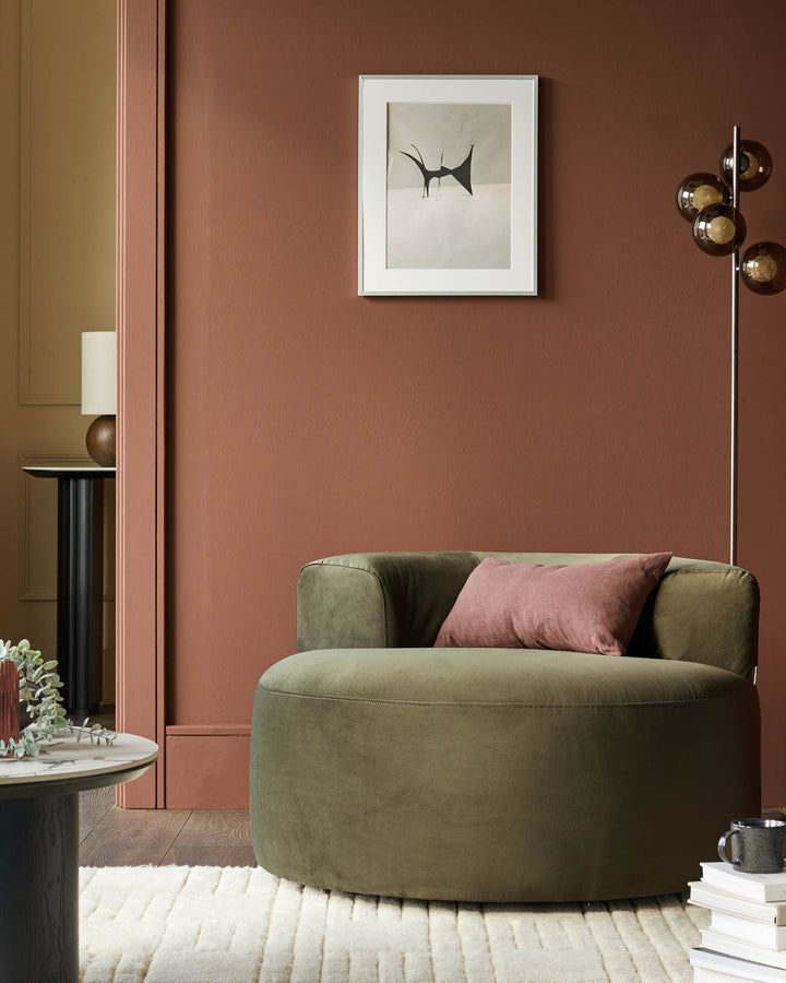 Stylish olive green swivel armchair with a pink cushion, complemented by a floor lamp and modern art.