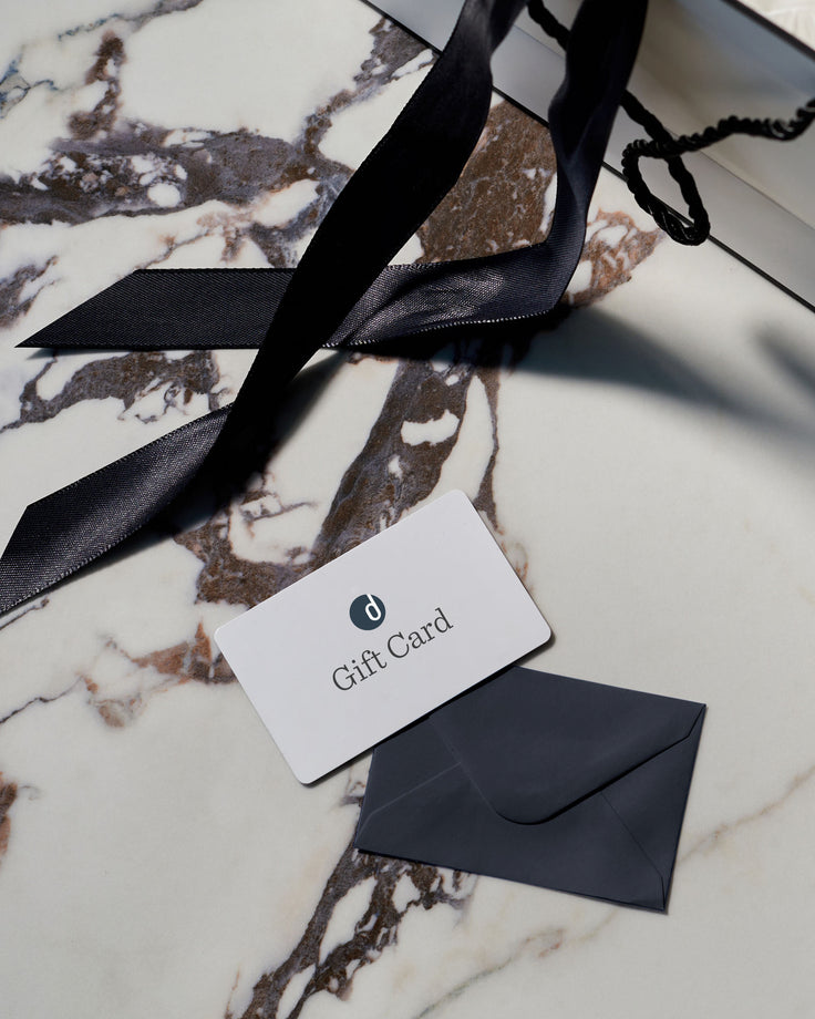 A gift card and envelope sit on a marble surface next to a partially visible shopping bag with a black ribbon handle.