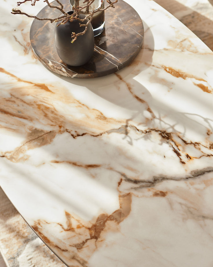A marble table with a stylish vase and decorative branches sits atop a coordinating marble tray, creating a sophisticated look.