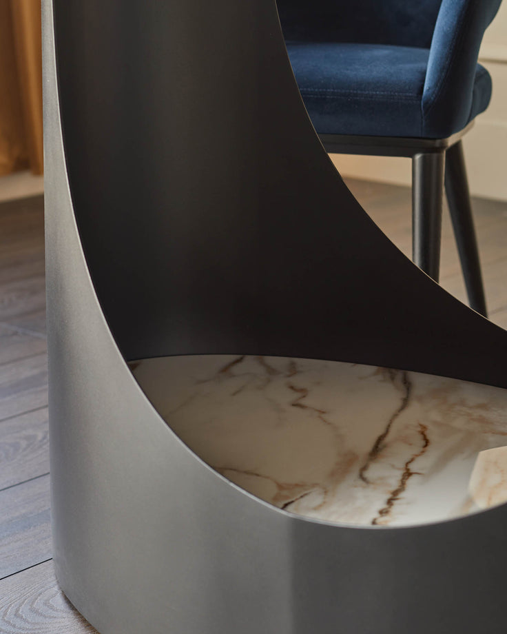 Close-up of a stylish grey side table with a marble-effect top, and a blue velvet chair in the background.