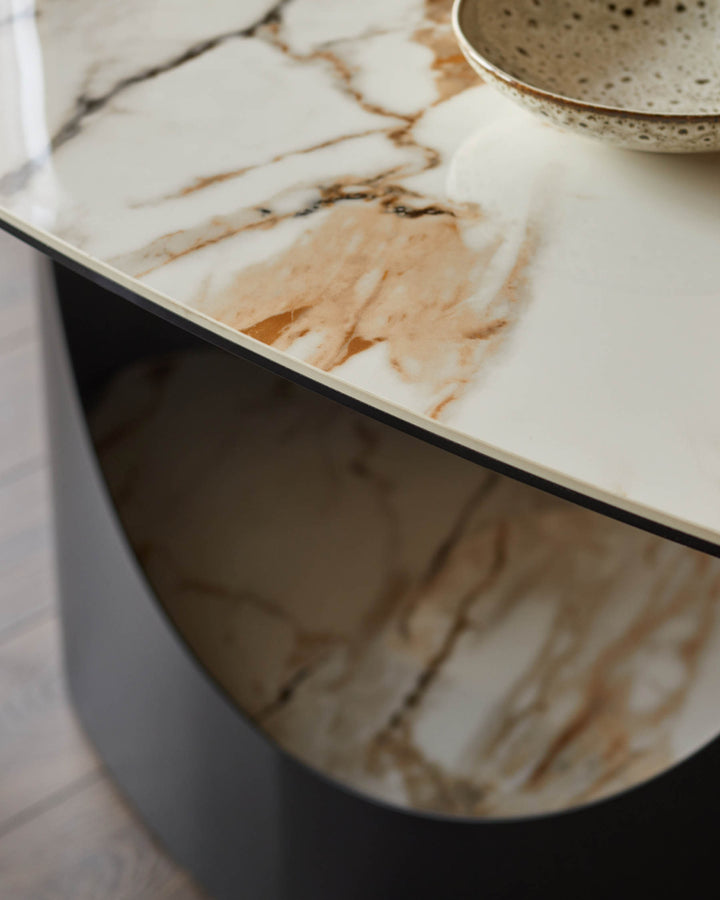 Close-up of a stylish marble-topped table with a contemporary black base and a decorative bowl on top.