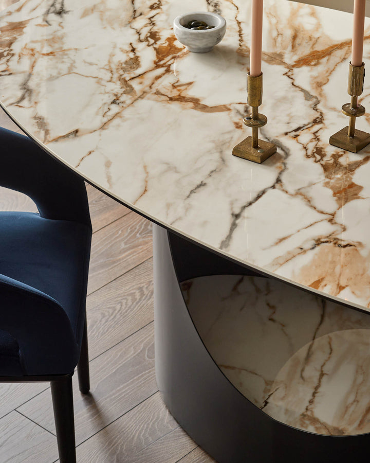 Close-up of a marble-topped dining table with brass candlesticks and a blue velvet chair. Elegant and modern.