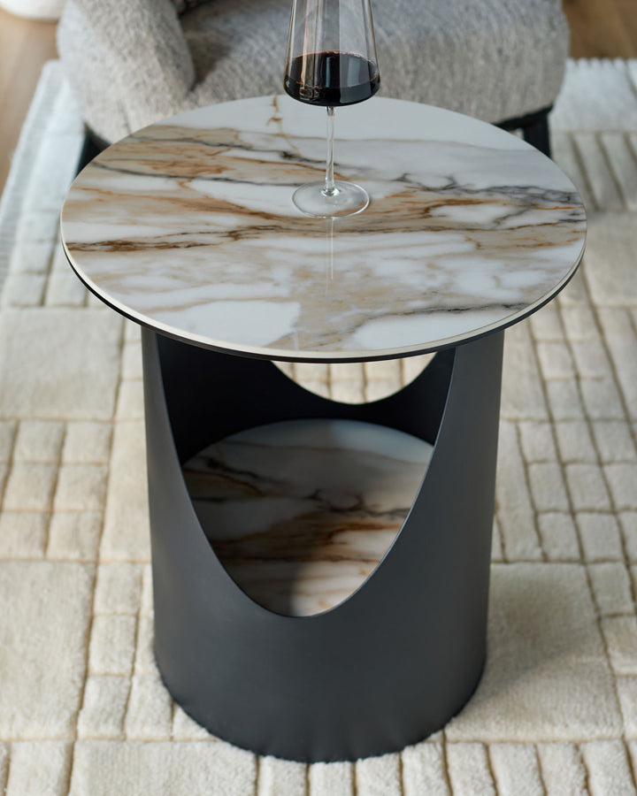 Giotto side table in black ceramic with marble-effect top, cylindrical base with curved cutout detail, pendant light above.