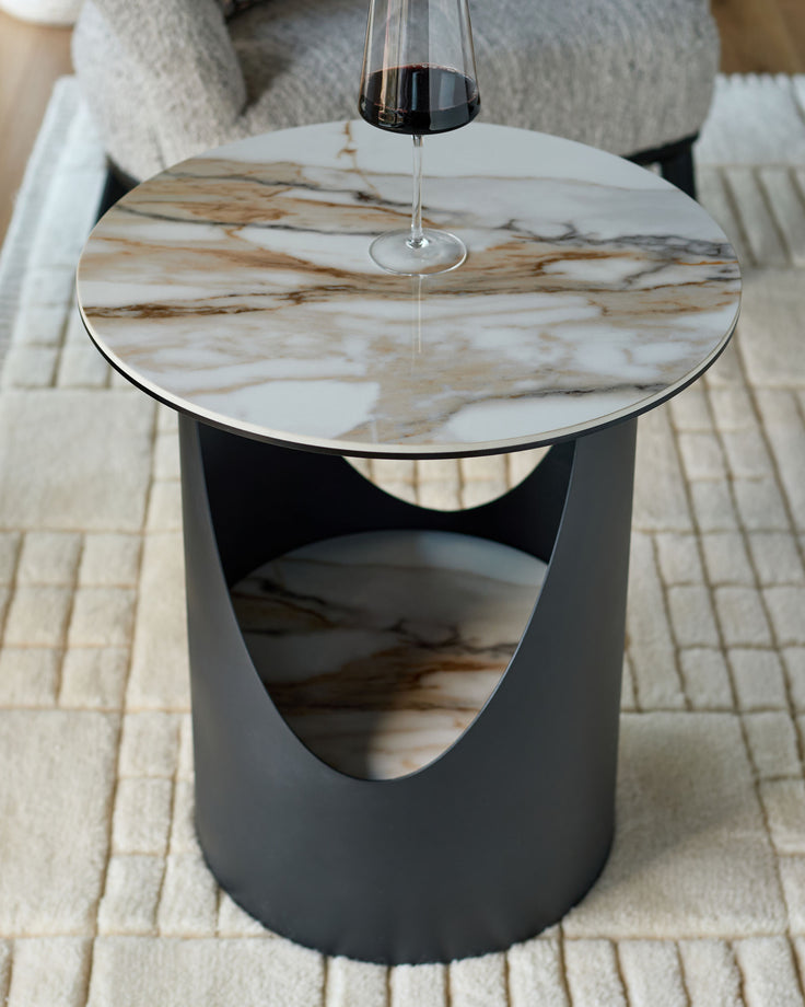Giotto side table in black ceramic with marble-effect top, cylindrical base with curved cutout detail, pendant light above.