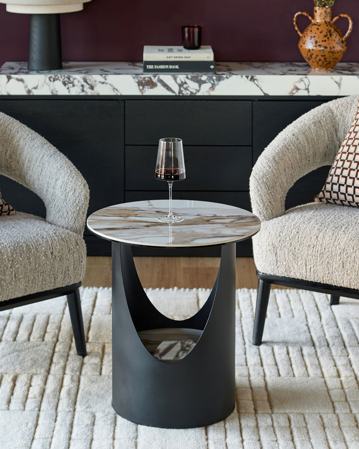Giotto side table in natural ceramic with round marble-effect top and cylindrical black base, styled in modern living room setting.