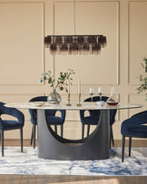 A modern dining set with a round table, blue velvet chairs and a statement chandelier, sat on an abstract patterned rug.