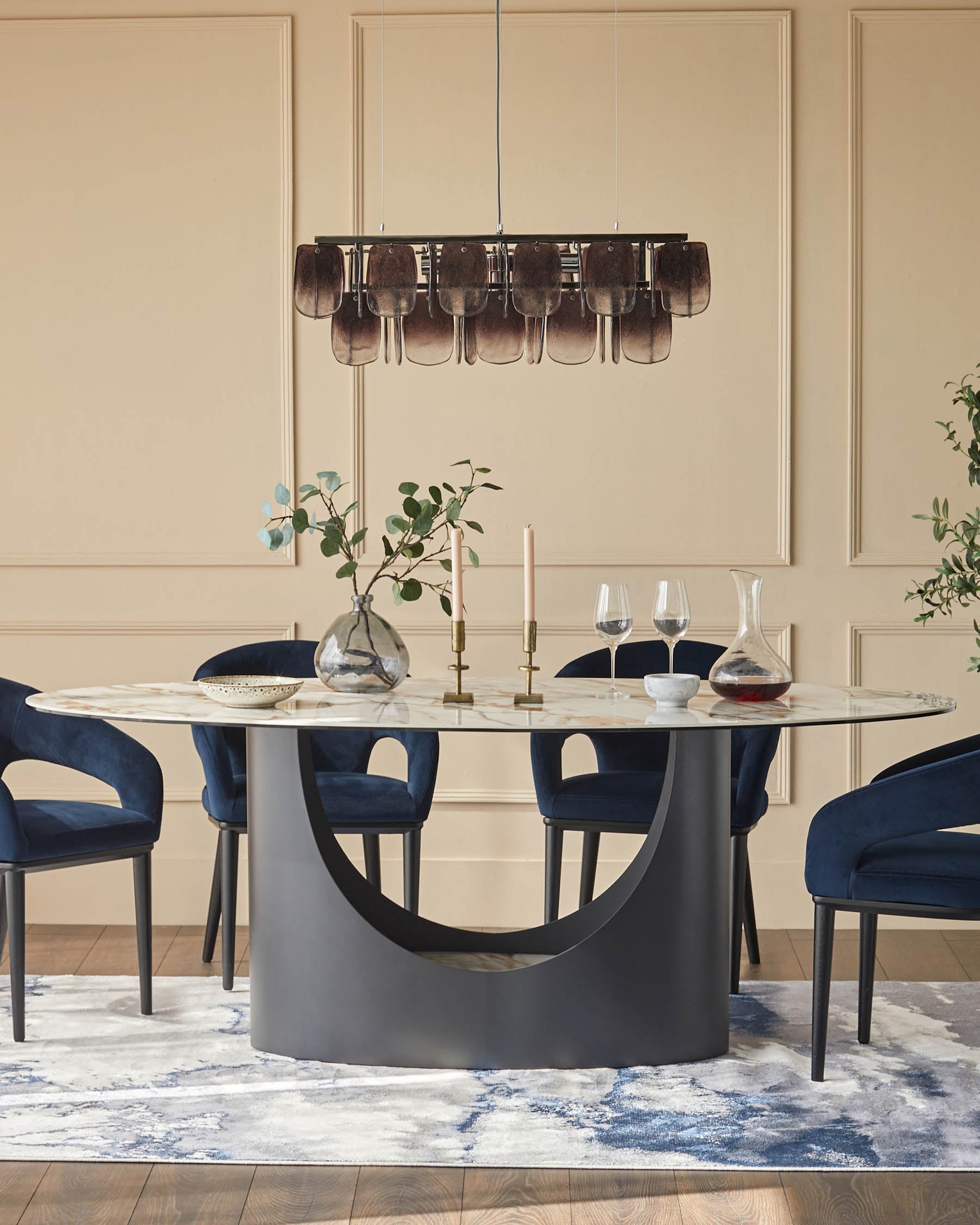 A modern dining set with a round table, blue velvet chairs and a statement chandelier, sat on an abstract patterned rug.