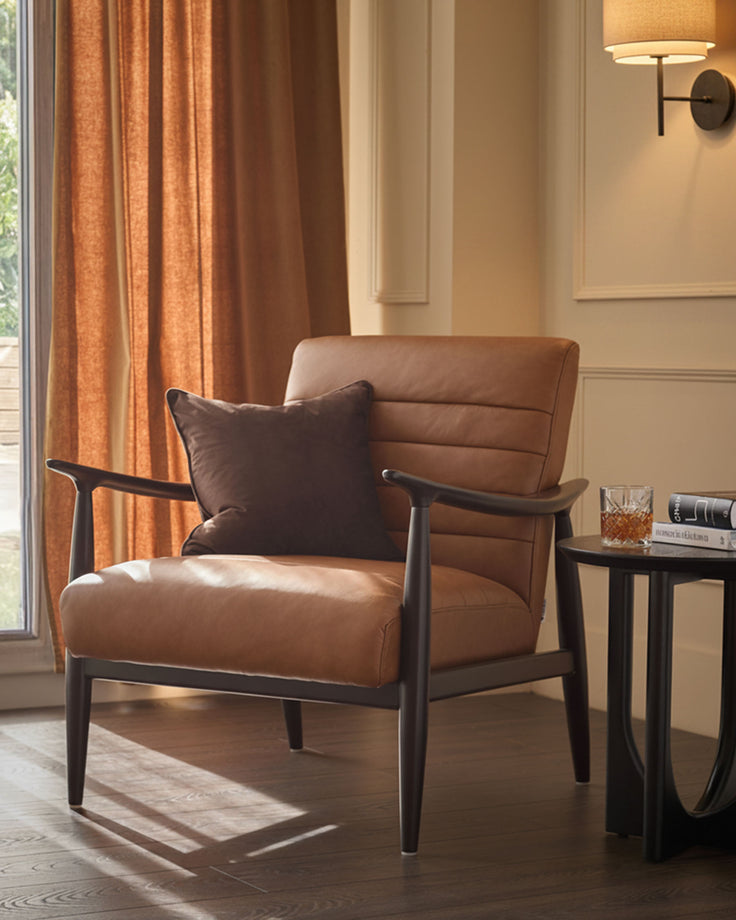 Tan leather accent chair with dark wood frame and armrests, paired with side table in modern living room setting.