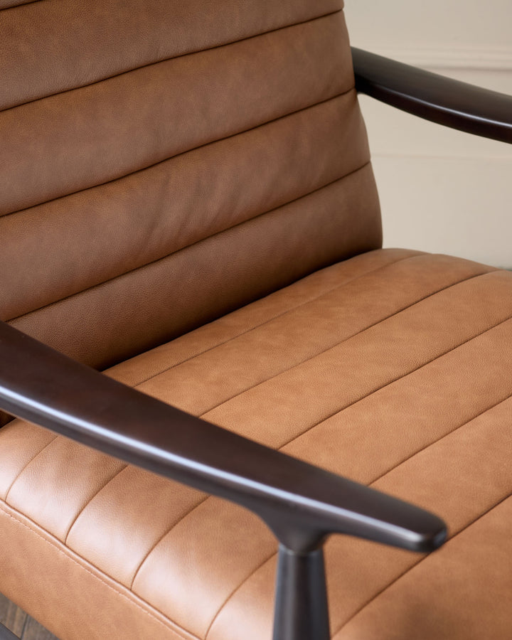 Greyson tan leather accent chair with black frame, showing quilted backrest and seat detail from side angle.