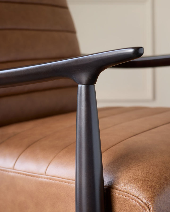 Close-up of dark metal armrest and tan leather seat of Greyson accent chair, showing curved design and stitching detail.
