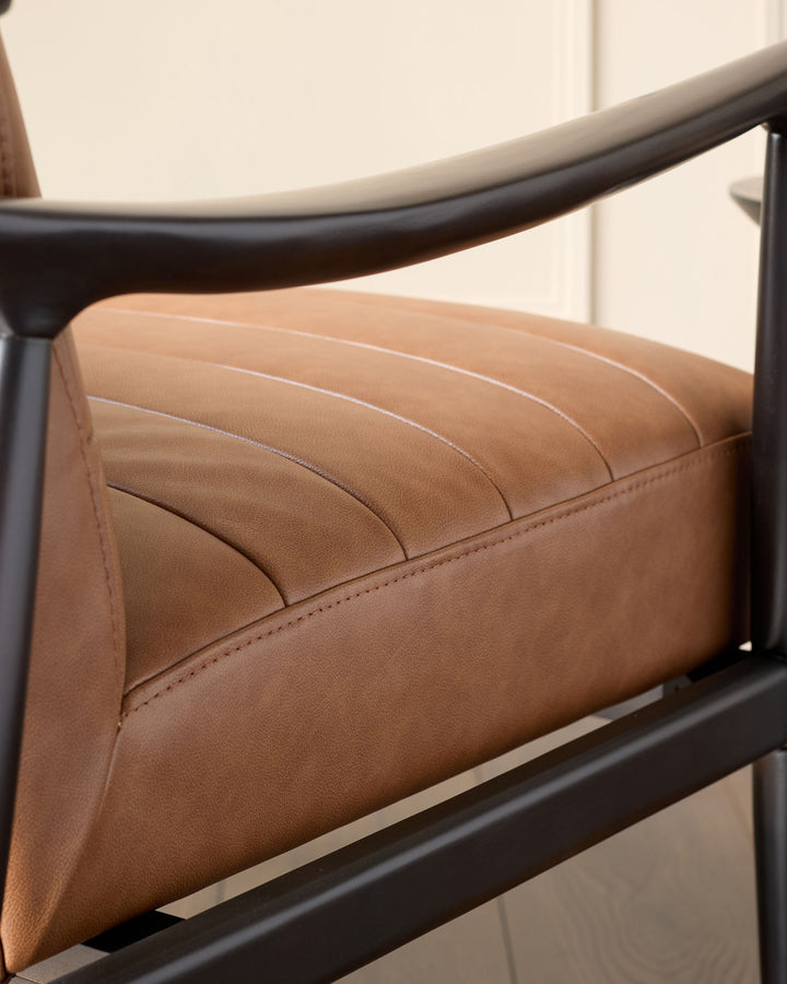 Greyson leather accent chair in tan with black metal frame and curved armrest, angled side view.