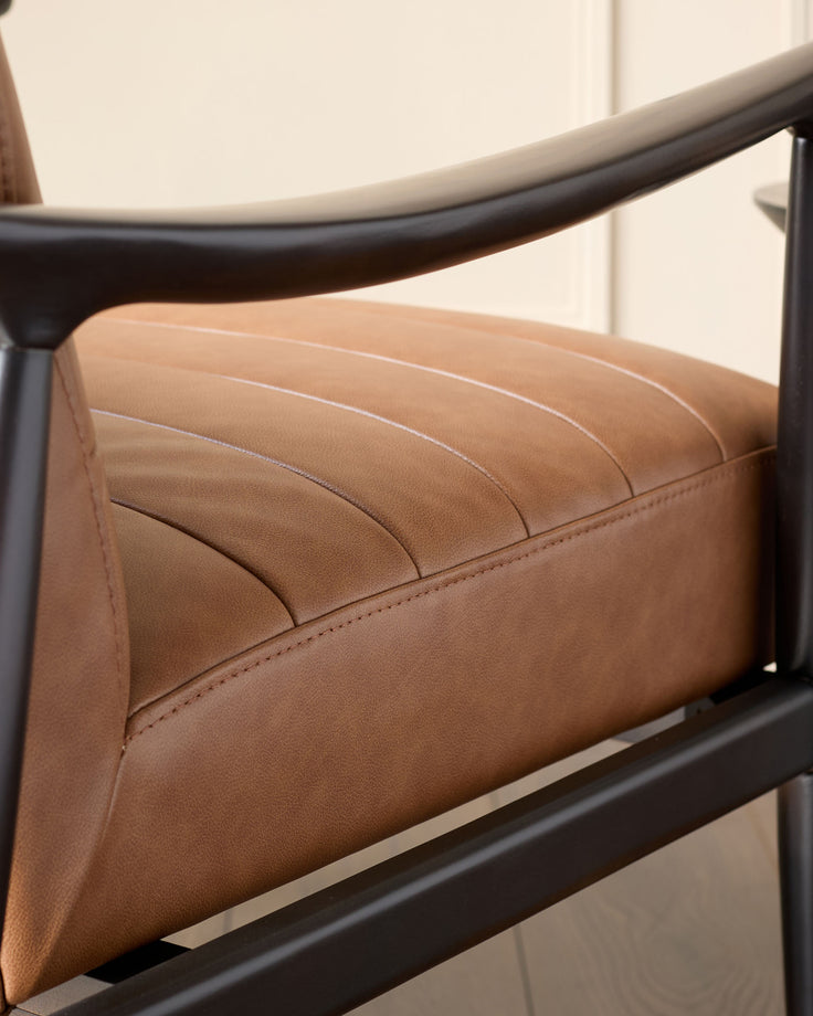 Greyson leather accent chair in tan with black metal frame and curved armrest, angled side view.