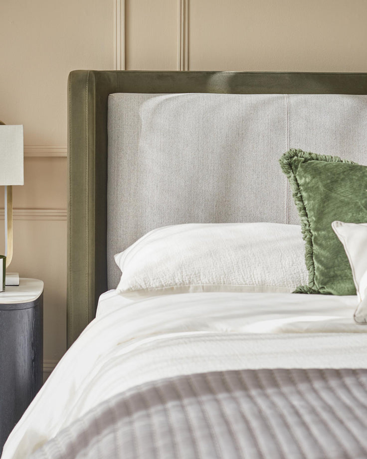 Bedroom with olive and neutral coloured bedding and headboard, next to a small side table and lamp.