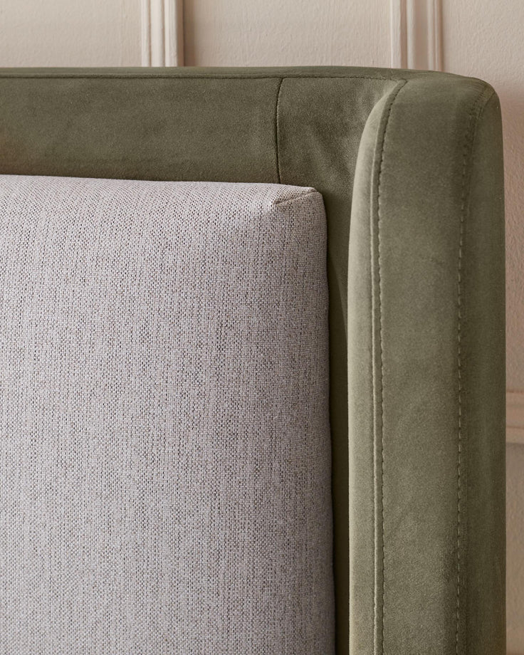 Close-up of a neutral cushion and a moss-green upholstered headboard with piped edge detailing.