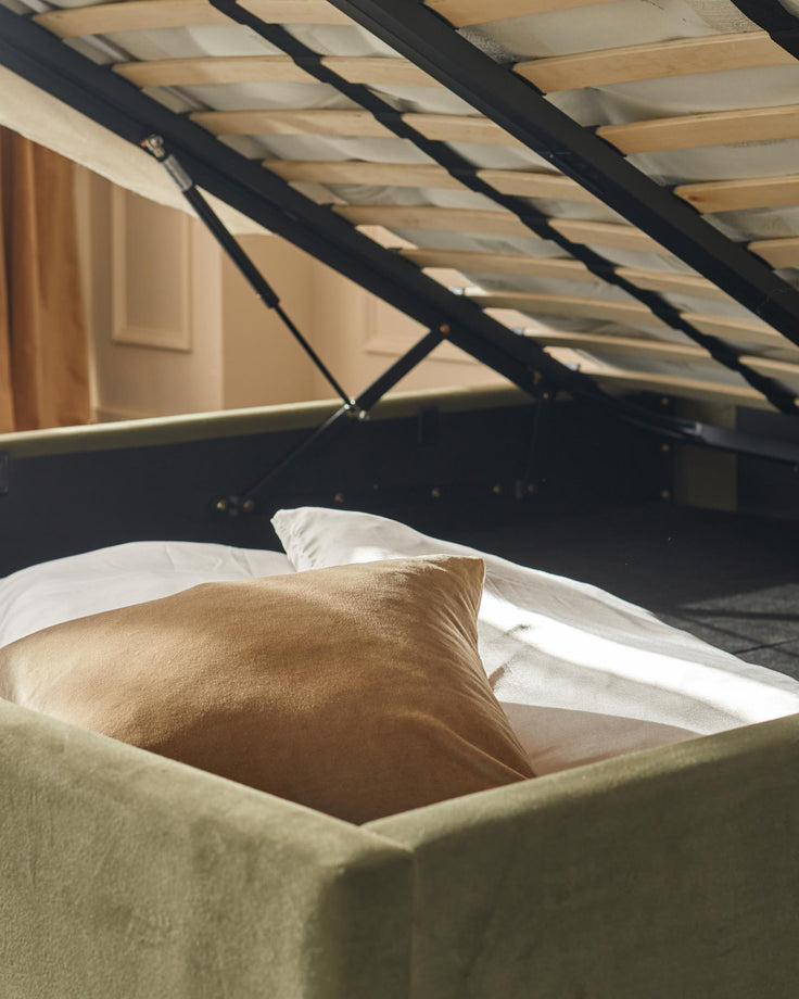 Storage bed frame with lift-up slats, revealing space underneath. Pillows on top of the bed.