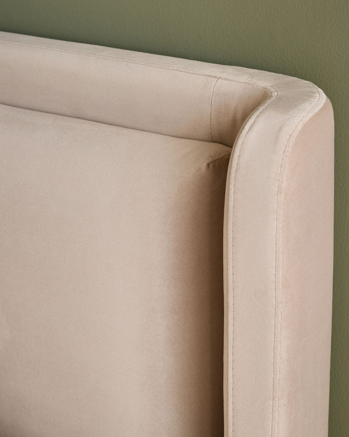 Close-up of champagne velvet upholstery and curved arm detail on Grove King Ottoman Bed against sage green wall.