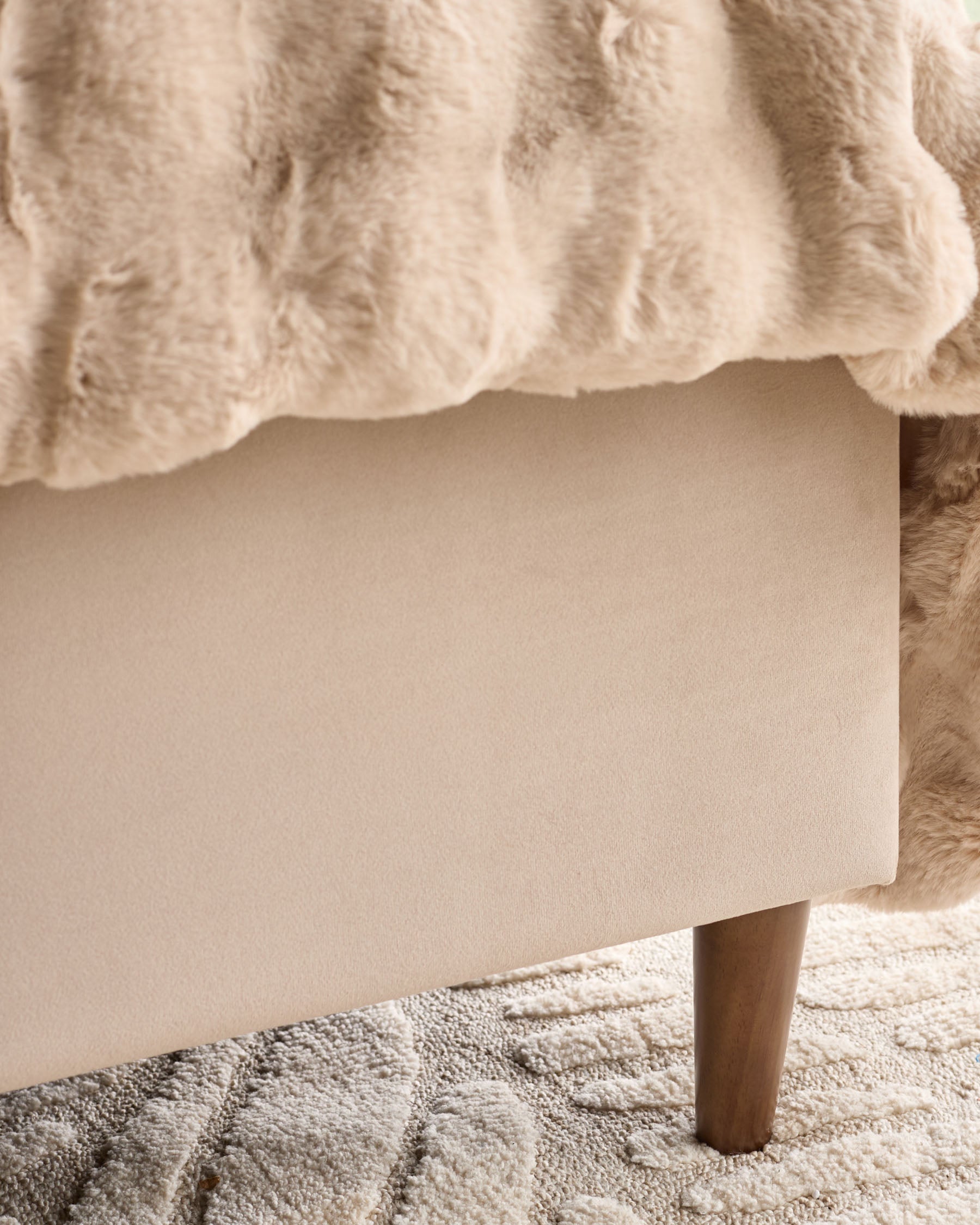 Grove King Ottoman Bed in champagne velvet, showing upholstered base with wooden leg on neutral rug.