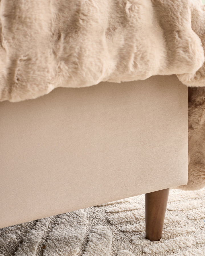 Grove King Ottoman Bed in champagne velvet, showing upholstered base with wooden leg on neutral rug.