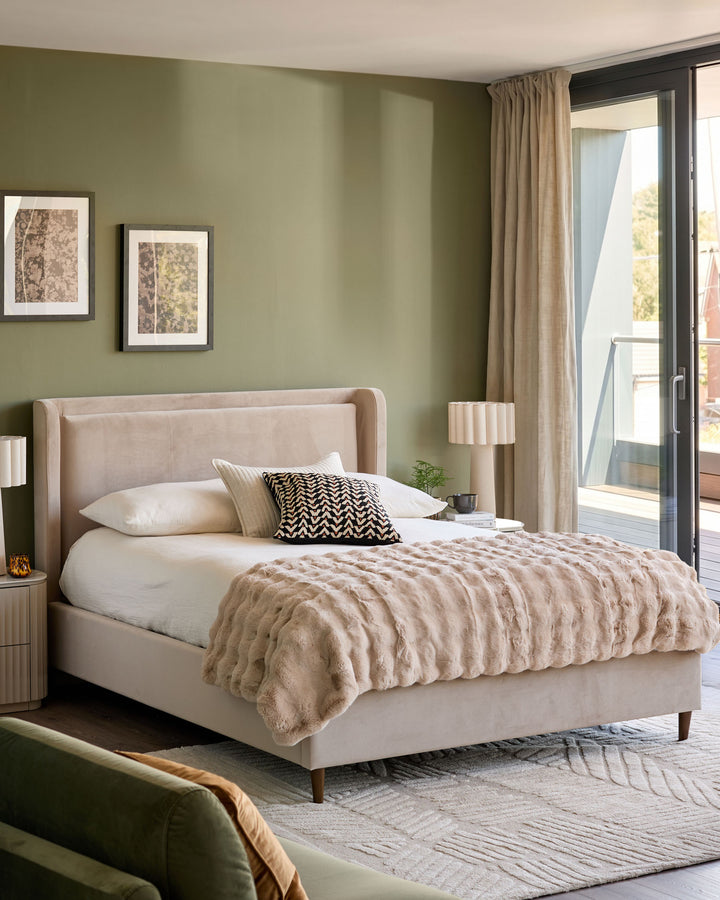 Grove King Ottoman Bed in champagne velvet, displayed in a sage green bedroom with matching nightstand and bedding.