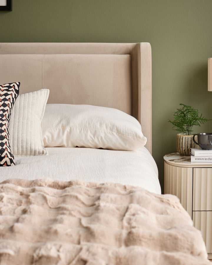 Champagne velvet upholstered bed with winged headboard, styled with white bedding and decorative pillows in a bedroom setting.