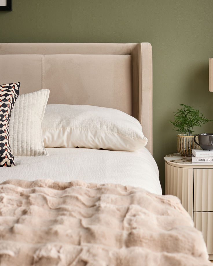 Champagne velvet upholstered bed with winged headboard, styled with white bedding and decorative pillows in a bedroom setting.