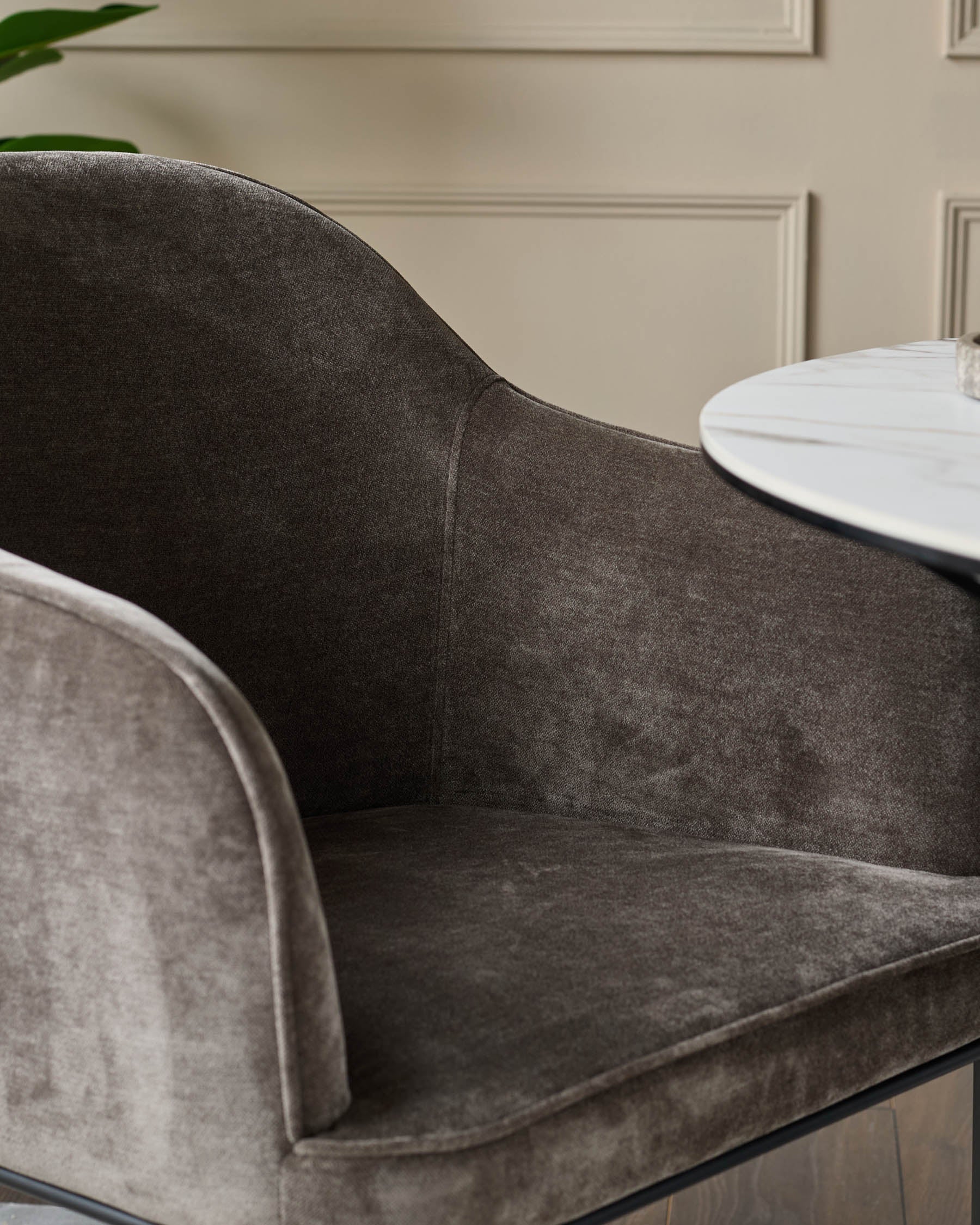 Close-up of a stylish brown upholstered chair with curved arms and a white marble-effect table top in the background.